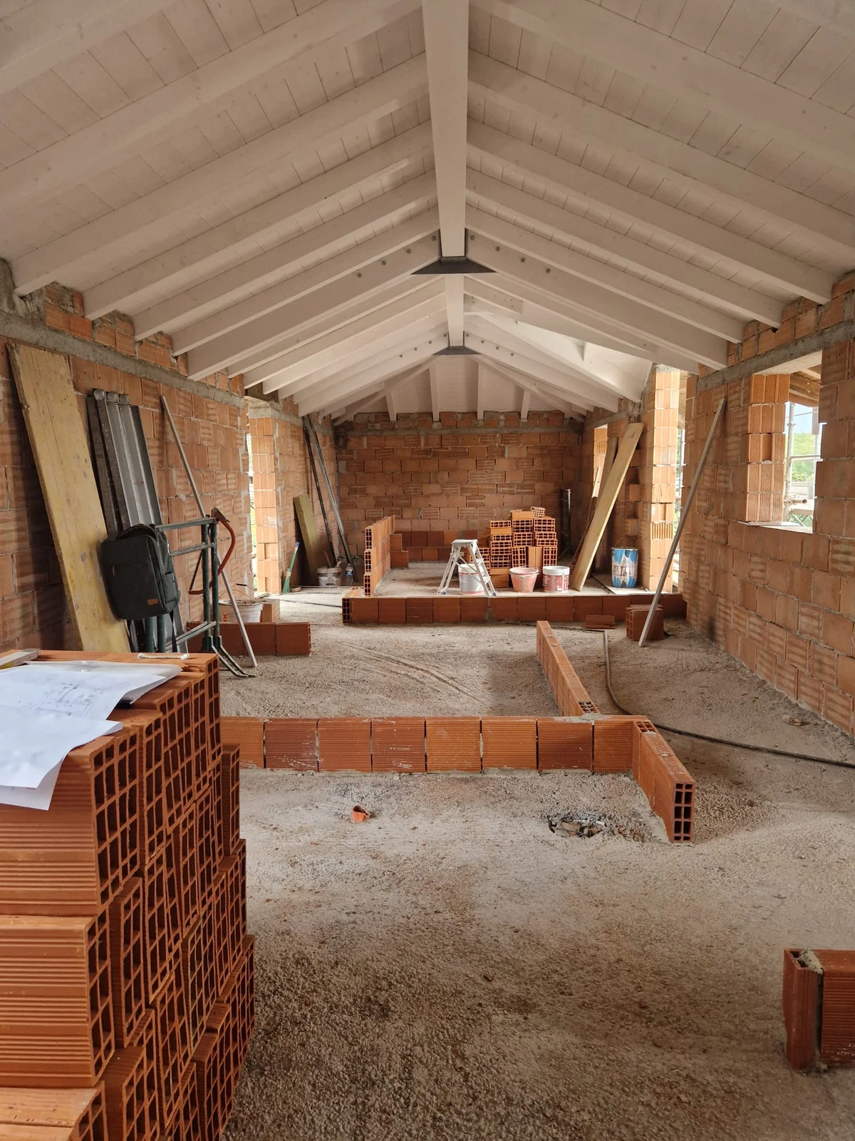 Interno in costruzione con murature in laterizio e copertura a falde con travi bianche